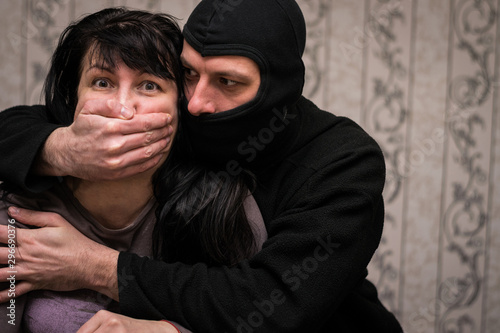A man in a black mask covers his mouth with a frightened woman. The thug takes a girl hostage. Maniac attacks man. Terrorist captures the victim. Criminal concept.