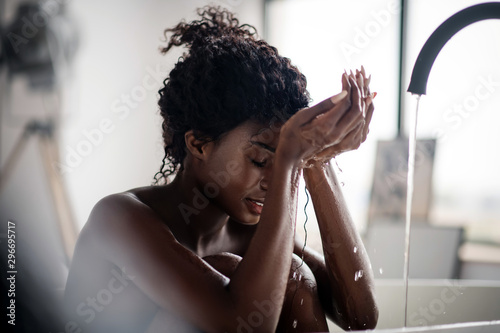 Curly woman having water drops on her face while washing it