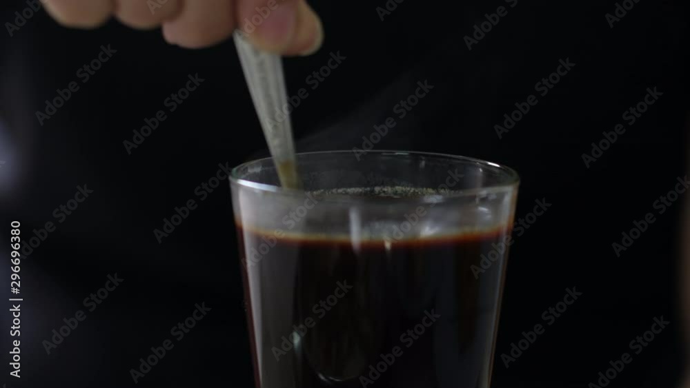close up of person hand stirring black coffee tea with spoon on black background in the morning. close up of person hand stirring black coffee tea with spoon on black background in the morning.