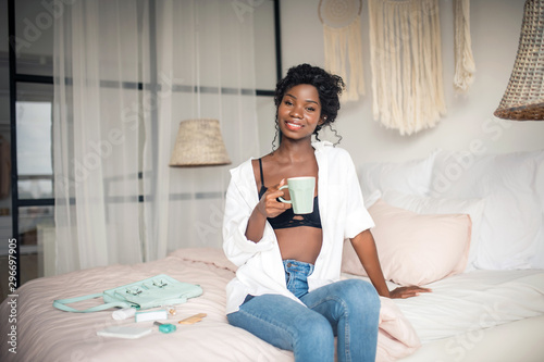 Dark-skinned woman wearing white blouse holding cup of coffee