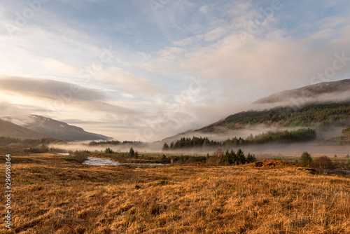 Sun is setting as low hanging clouds run through the River Orchy, a pine forest and the hills in the distance on a partially cloudy day in the Highlands of Scotland.,Blue, Brown, Clouds, Color, Colour