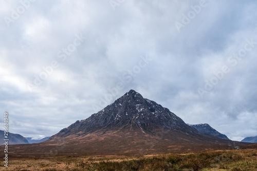 Wintery brown grass fields overlooks Buachaille Etive Mòr mountain on a cloudy day in the Scottish Highlands.
