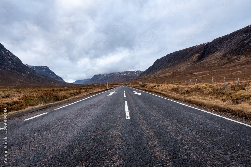 Road going towards Glencoe with arrows, lines and a car in the distance on a cloudy day in the Scottish Highlands. Road going towards Glencoe with arrows, lines and a car in the distance on a cloudy day in the Scottish Highlands.