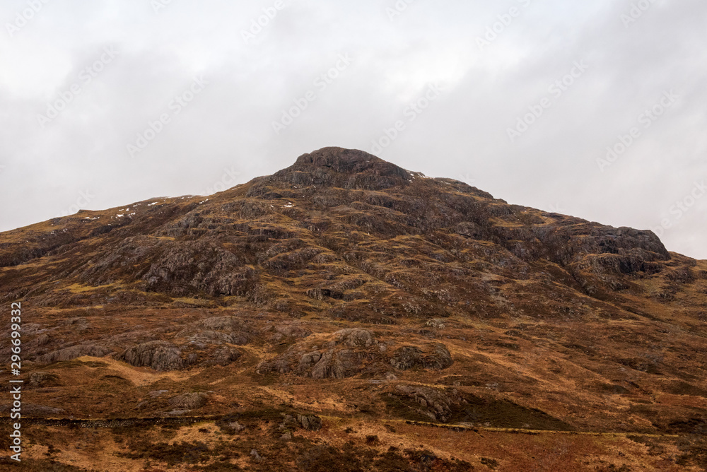 A hill in the Scottish Highlands covered in brown wintery grass on a cloudy and grey day.