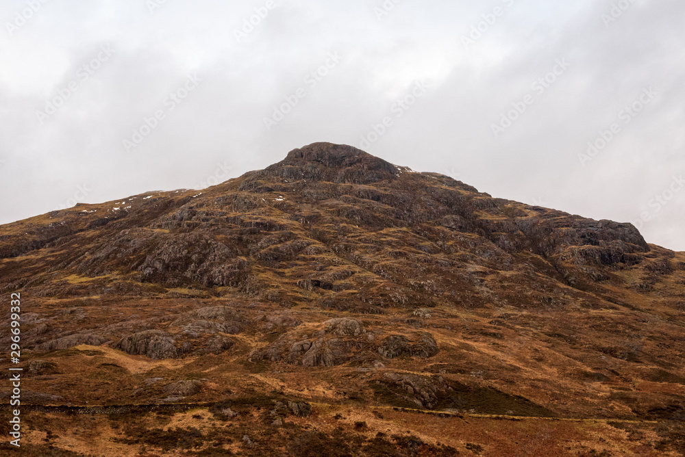 A hill in the Scottish Highlands covered in brown wintery grass on a cloudy and grey day. A hill in the Scottish Highlands covered in brown wintery grass on a cloudy and grey day.