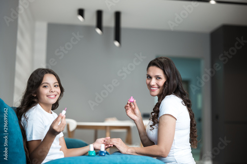 beautiful young mother and her cute smiling teen daughter doing manicure applying nail polish both having fun