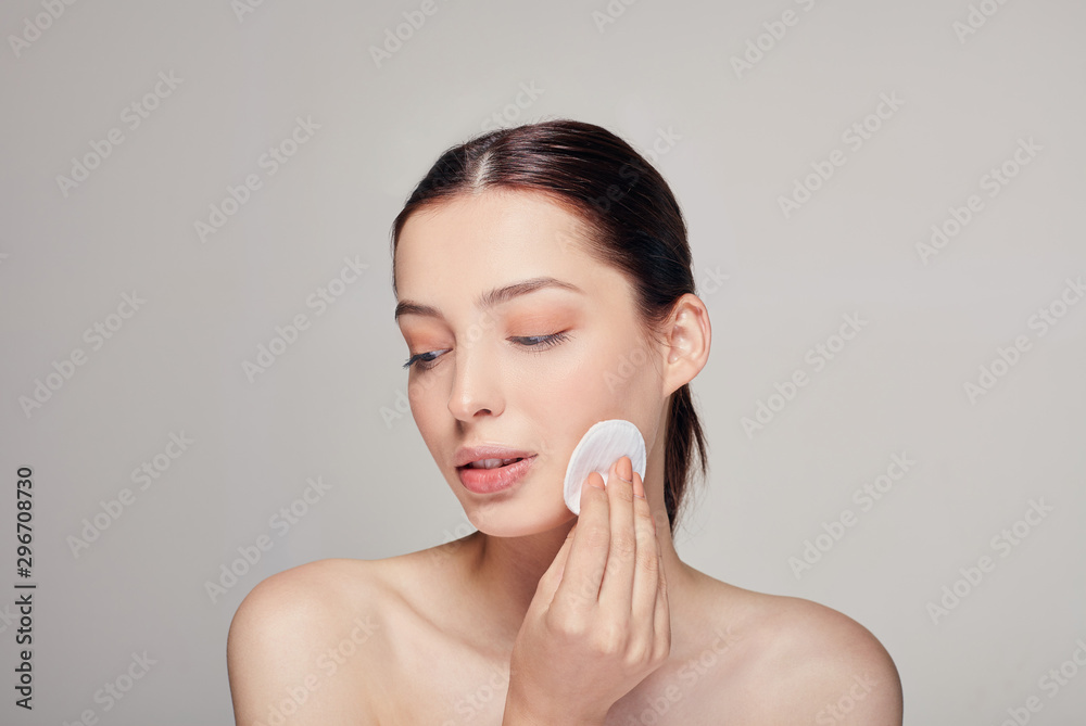 Close-up young beautiful tender calm girl with a cotton pad in in her right hand looks away thinking on the background Close-up young beautiful tender calm girl with a cotton pad in in her right hand looks away thinking on the background