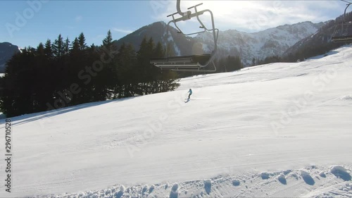 Shot from a ski lift going uphill with skiers in the background of snowy mountain peaks and skiers going downhill