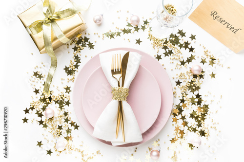 Christmas elegance table setting with pink dishware, golden silverware on white background. Top view. Xmas dinner. Table reserved.