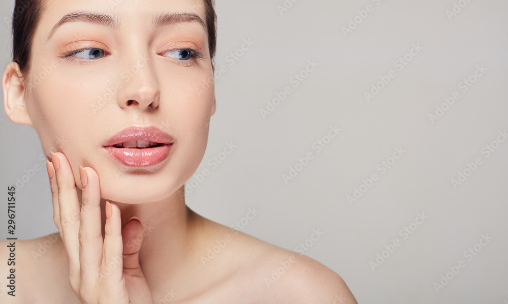 Beautiful young woman with clean fresh skin touch her own face with her right hand looking side. Beauty and spa. Face care.