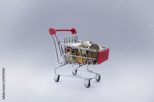 Coins in shopping cart. Banking and marketing. Shopping trolley with small coins. Red basket with coins on grey background. Shopping for the holiday. lack of money, rise in price of goods. retiree gr