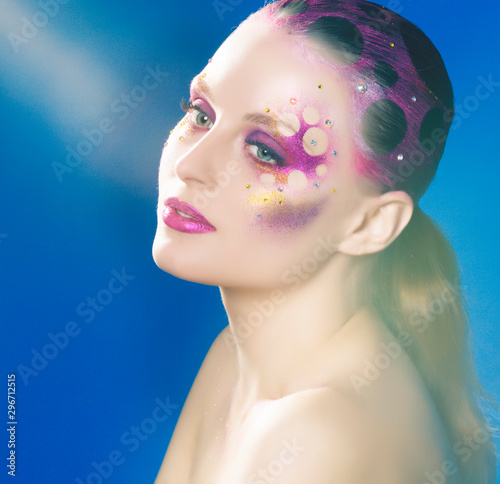 beauty young woman with creative fashion rhinestones make up on blue background, mystery tinsel holiday look