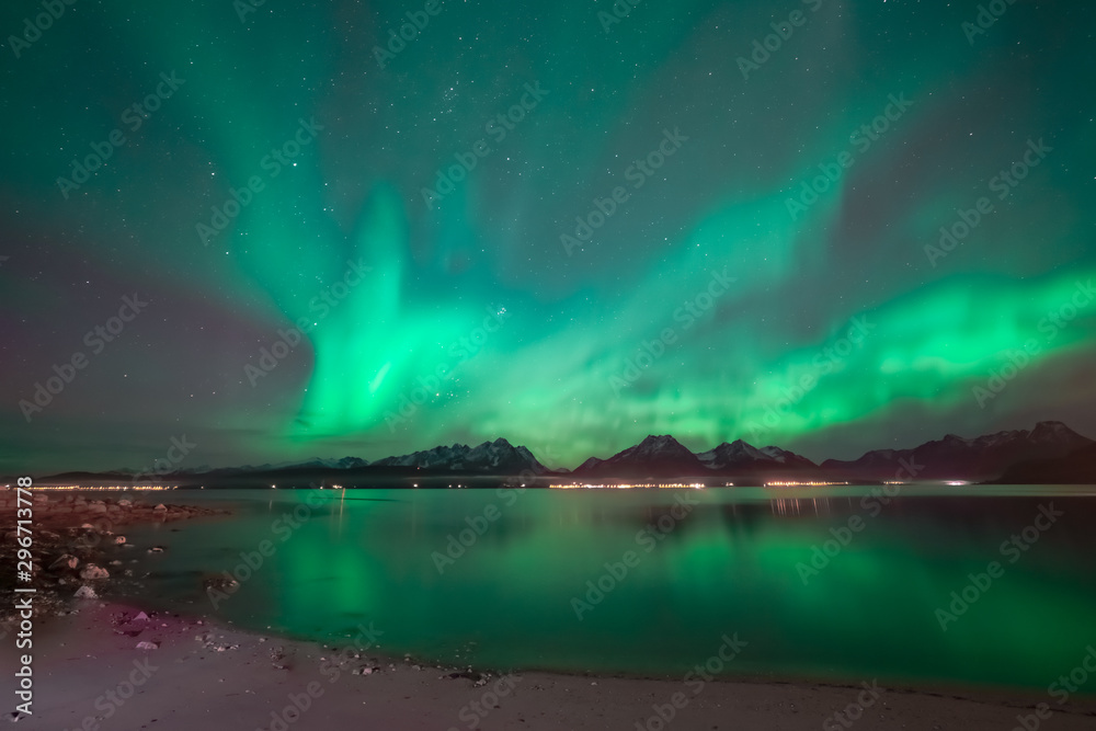 Aurora covering the sky above mountain range. In foreground sand beach. Northern lights reflects in the ocean.