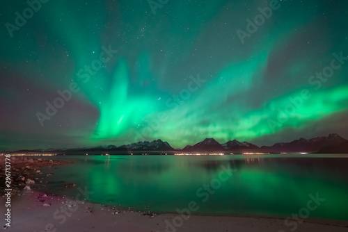 Aurora covering the sky above mountain range. In foreground sand beach. Northern lights reflects in the ocean. © Ida Haugaard Olsen