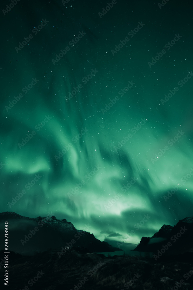 Green aurora above dark mountain landscape. Northern ligths covering the sky.  Ersfjordbotn, Tromso, Norway.