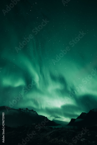 Green aurora above dark mountain landscape. Northern ligths covering the sky. Ersfjordbotn, Tromso, Norway.