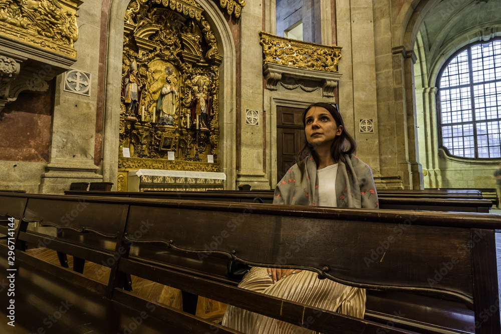 A believing woman sits on a bench in the church and prays to God. Girl praying in a church of Clerigos in Porto