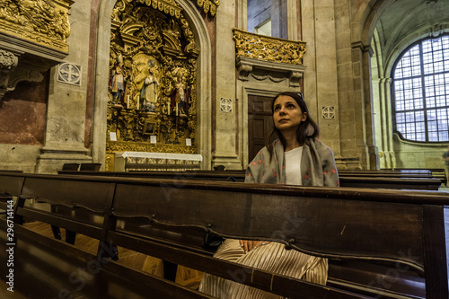 A believing woman sits on a bench in the church and prays to God. Girl praying in a church of Clerigos in Porto