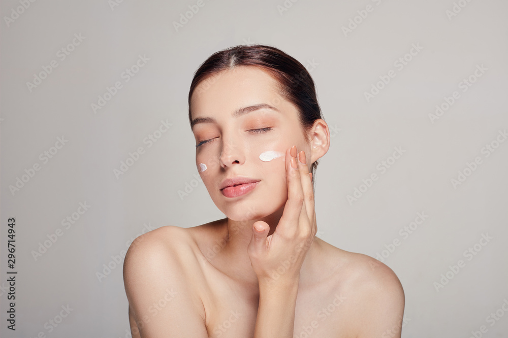 Young beautiful woman with closed eyes is applying cosmetic cream on her face. Cream on the cheeks.Skin care. Dry skin. Beauty concept. Young beautiful woman with closed eyes is applying cosmetic cream on her face. Cream on the cheeks.Skin care. Dry skin. Beauty concept.