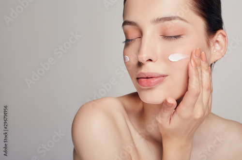 Beauty concept. Young beautiful woman with closed eyes is applying cosmetic cream on her face. Home care. Skin care. Dry skin.