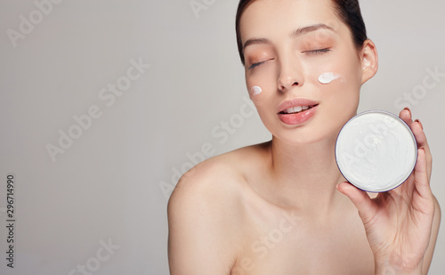 Young beautiful woman with dark hair and closed eyes holds face cream in her left hand. Face cream woman beauty portrait.