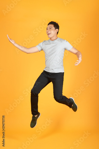 Full length portrait of an excited young man in white t-shirt jumping while celebrating success isolated over orange background © makistock
