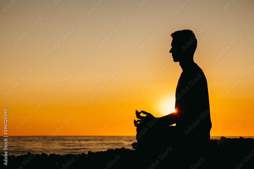 Silhouette of a man in meditation pose on beach on sea background and sunset. Concept of freedom relaxation. Place for text or advertising