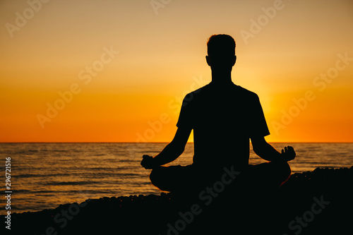 Silhouette of a man in meditation pose on beach on sea background and sunset. Concept of freedom relaxation. Place for text or advertising © Andriy