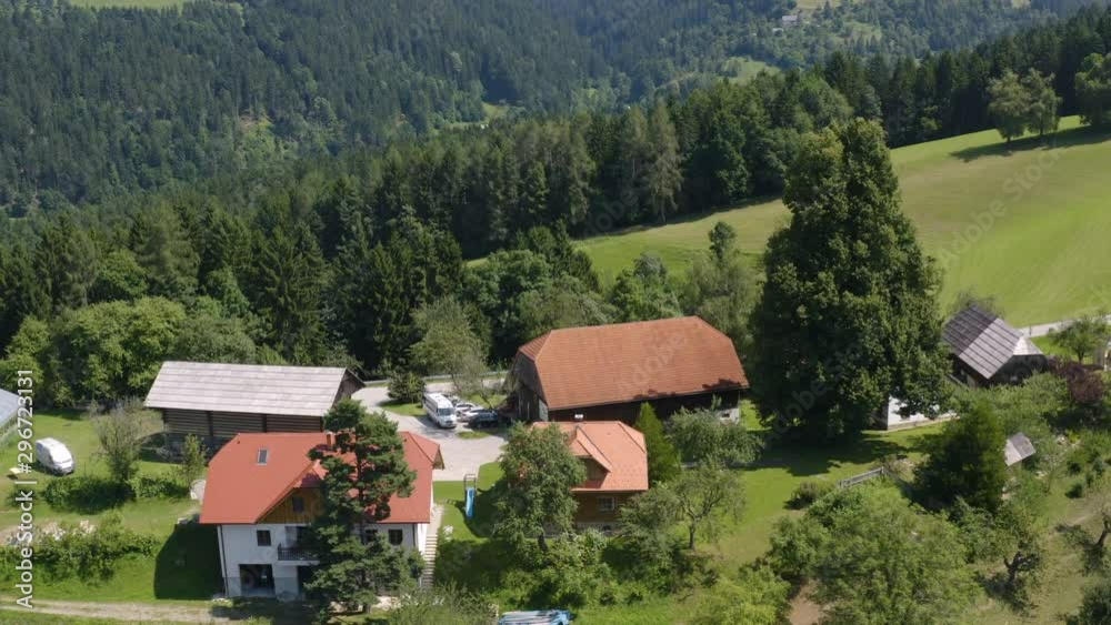 Aerial pan shot above the small remote farm house on top of a hill surrounded by forest and meadows in rural Slovenia on a sunny day Aerial pan shot above the small remote farm house on top of a hill surrounded by forest and meadows in rural Slovenia on a sunny day