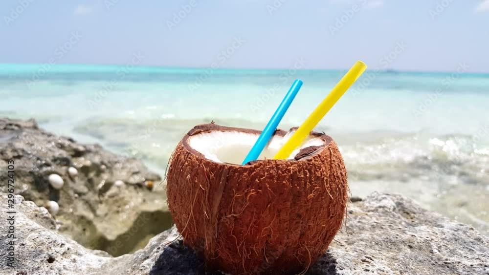 Static close up shot of a coconut with two straws sitting on a rock next to a tropical beach with the waves crashing on the shore in Thailand 4K Static close up shot of a coconut with two straws sitting on a rock next to a tropical beach with the waves crashing on the shore in Thailand 4K
