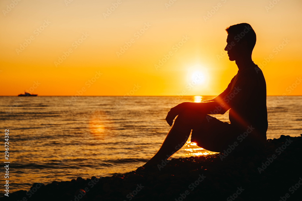 Silhouette of a man sitting and contemplating on beach on sea background and sunset. Concept of freedom relaxation. Place for text or advertising