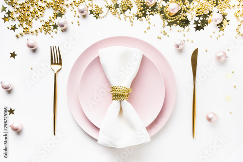 Christmas table setting with pink dishware, golden silverware and party decorations on white background. Top view. Xmas dinner.
