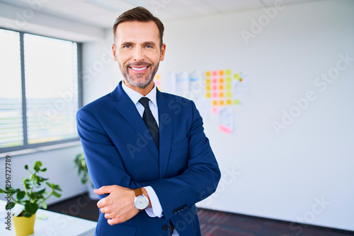 Photo Confident businessman smiling at camera with arms crossed while standing in offi