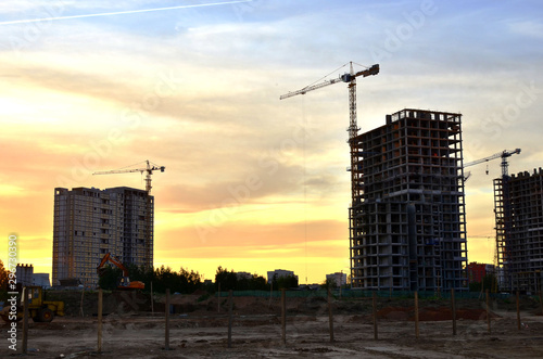 Jib construction tower crane and new residential buildings at a construction site on the sunset and blue sky background - Image