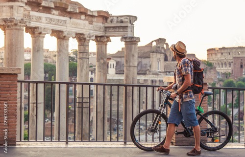 Canvas Print Young man tourist with backpack and bike walking at Roman Forum at sunrise