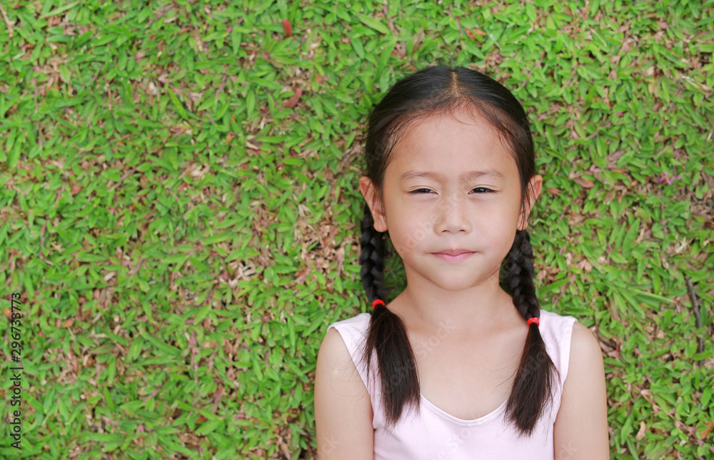 Portrait of beautiful little Asian child girl with two ponytail hair lying on green grass lawn. Portrait of beautiful little Asian child girl with two ponytail hair lying on green grass lawn.