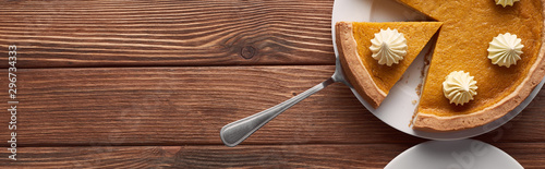 panoramic shot of delicious pumpkin pie with whipped cream on plate with spatula on brown wooden table photo