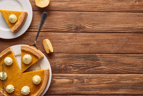 delicious pumpkin pie with whipped cream near cut apple on brown wooden table