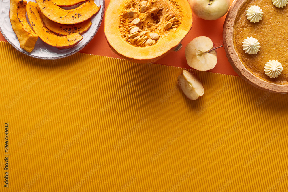 Fototapeta premium delicious pumpkin pie with whipped cream near sliced baked pumpkin, whole and cut apples, and textured napkin on orange surface