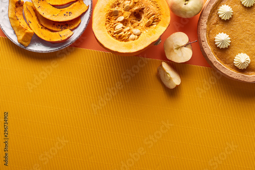 delicious pumpkin pie with whipped cream near sliced baked pumpkin, whole and cut apples, and textured napkin on orange surface