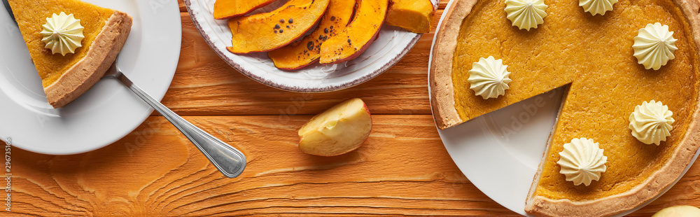 panoramic shot of delicious pumpkin pie with whipped cream near baked pumpkin and cut apple on orange wooden table panoramic shot of delicious pumpkin pie with whipped cream near baked pumpkin and cut apple on orange wooden table