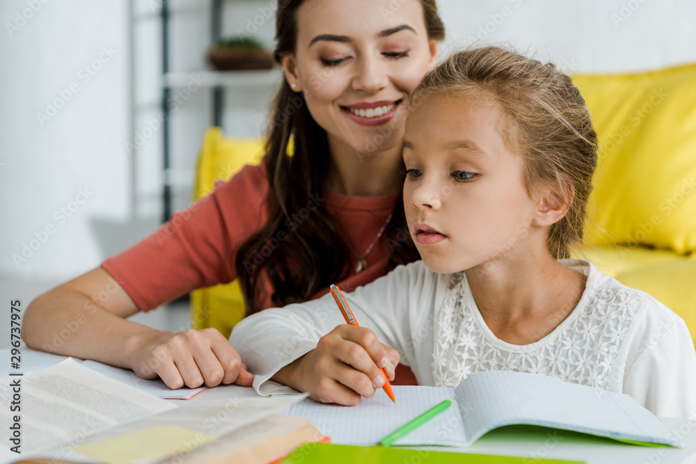 selective focus of cute kid studying near cheerful babysitter at home selective focus of cute kid studying near cheerful babysitter at home