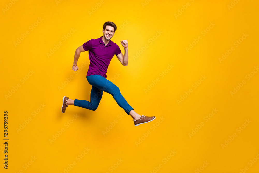 Full length body size phoo of cheerful brown haired attractive man wearing blue pants trousers purple t-shirt footwear aspiring jumping running isolated over yellow vivid color background