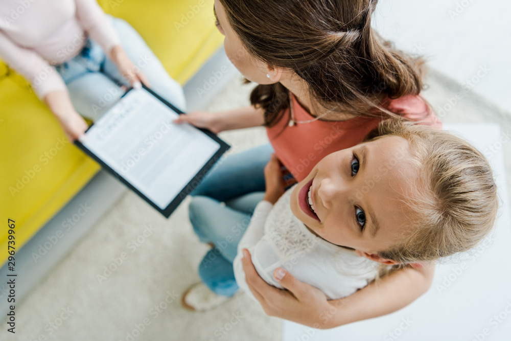 overhead view of mother standing with happy daughter and giving clipboard to babysitter overhead view of mother standing with happy daughter and giving clipboard to babysitter