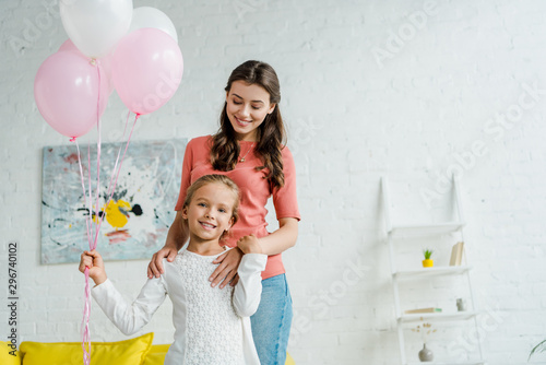 happy kid holding pink balloons near cheerful babysitter
