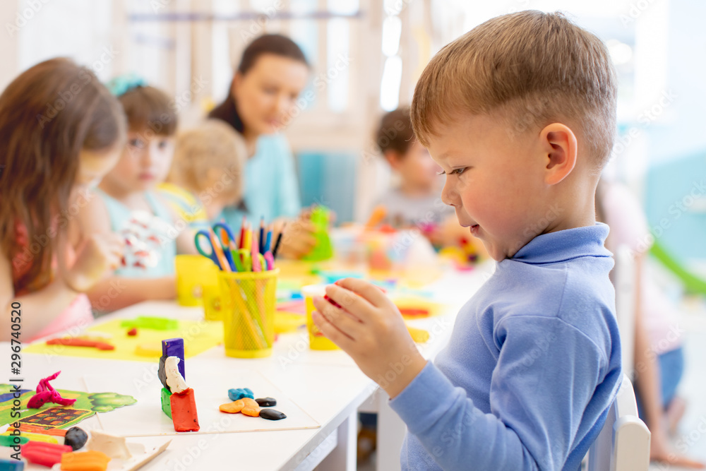 Child boy and group of kids working with colorful clay toy in nursery. Creative child molding in kindergarten. Preschoolers play with plasticine or dough. Child boy and group of kids working with colorful clay toy in nursery. Creative child molding in kindergarten. Preschoolers play with plasticine or dough.