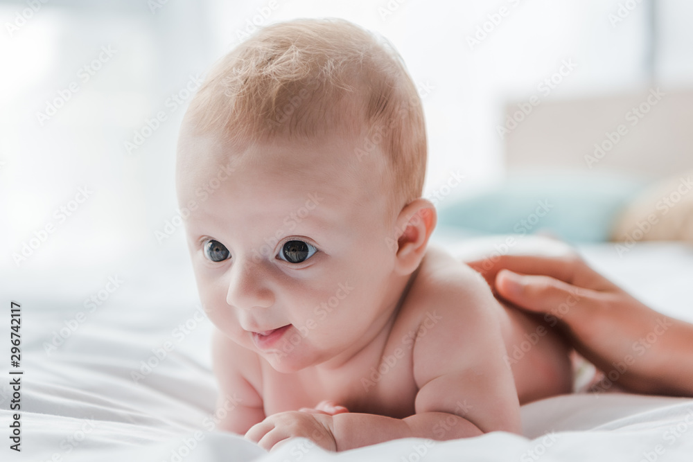 cropped view of woman touching cute baby daughter lying on bed cropped view of woman touching cute baby daughter lying on bed
