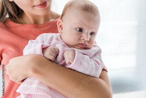 cropped view of smiling woman holding in arms adorable infant daughter at home