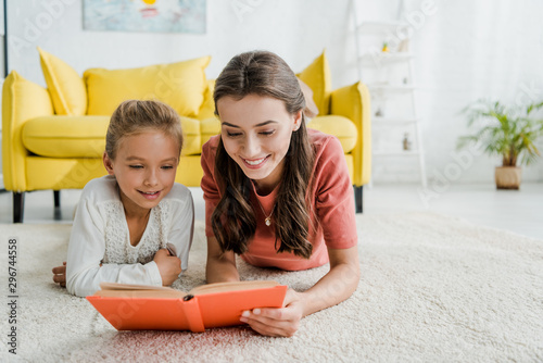happy babysitter lying on carpet with cheerful kid while reading book photo