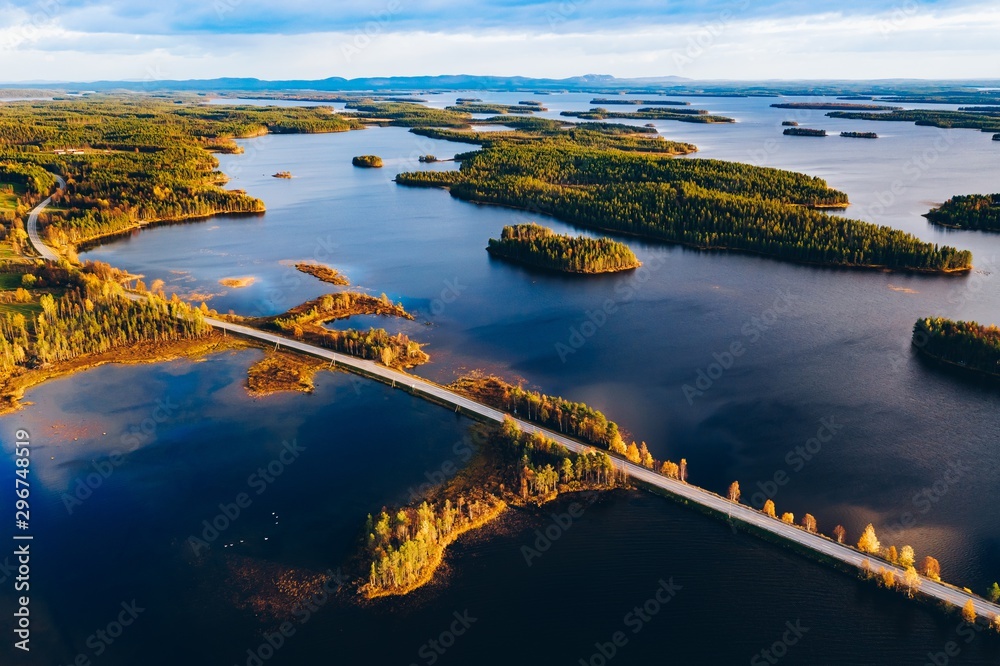 Aerial view of road bridge across blue lakes with islands and colorful autumn forest in Finland.